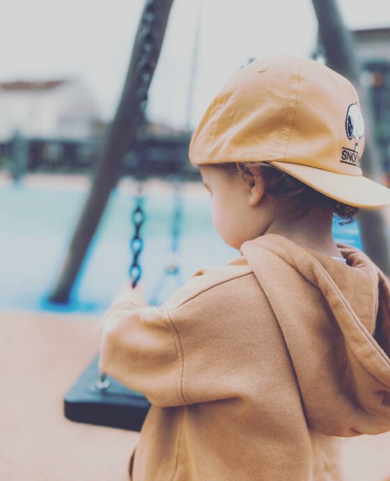 boy in brown coat and white cap sitting on bench during daytime
