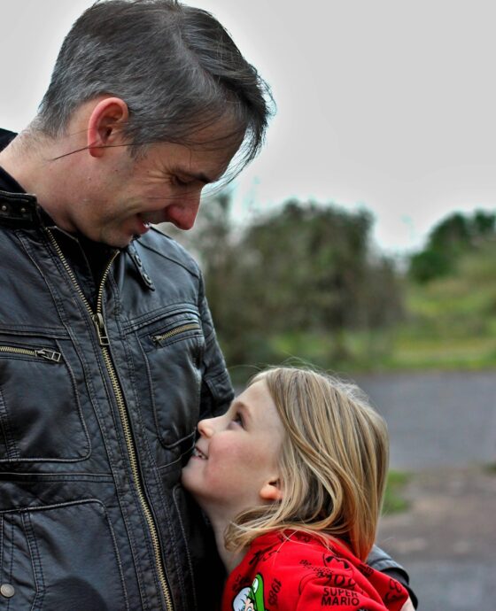 man in black leather jacket kissing woman in red hoodie during daytime